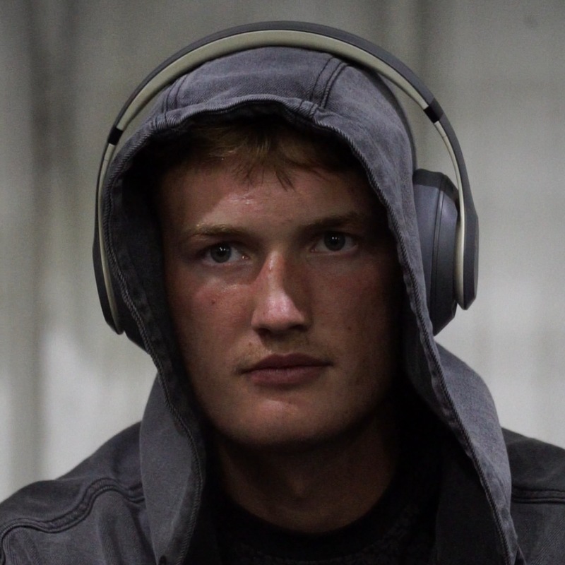 Colton Tidwell in a gray hoodie with the hood up and headphones on, looking into the camera.